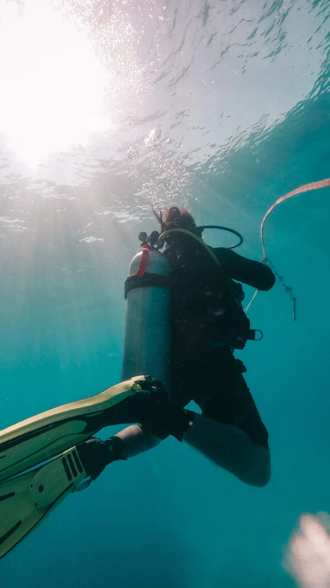 Scuba diver following a guideline as sunlight filters down through clear cenote water