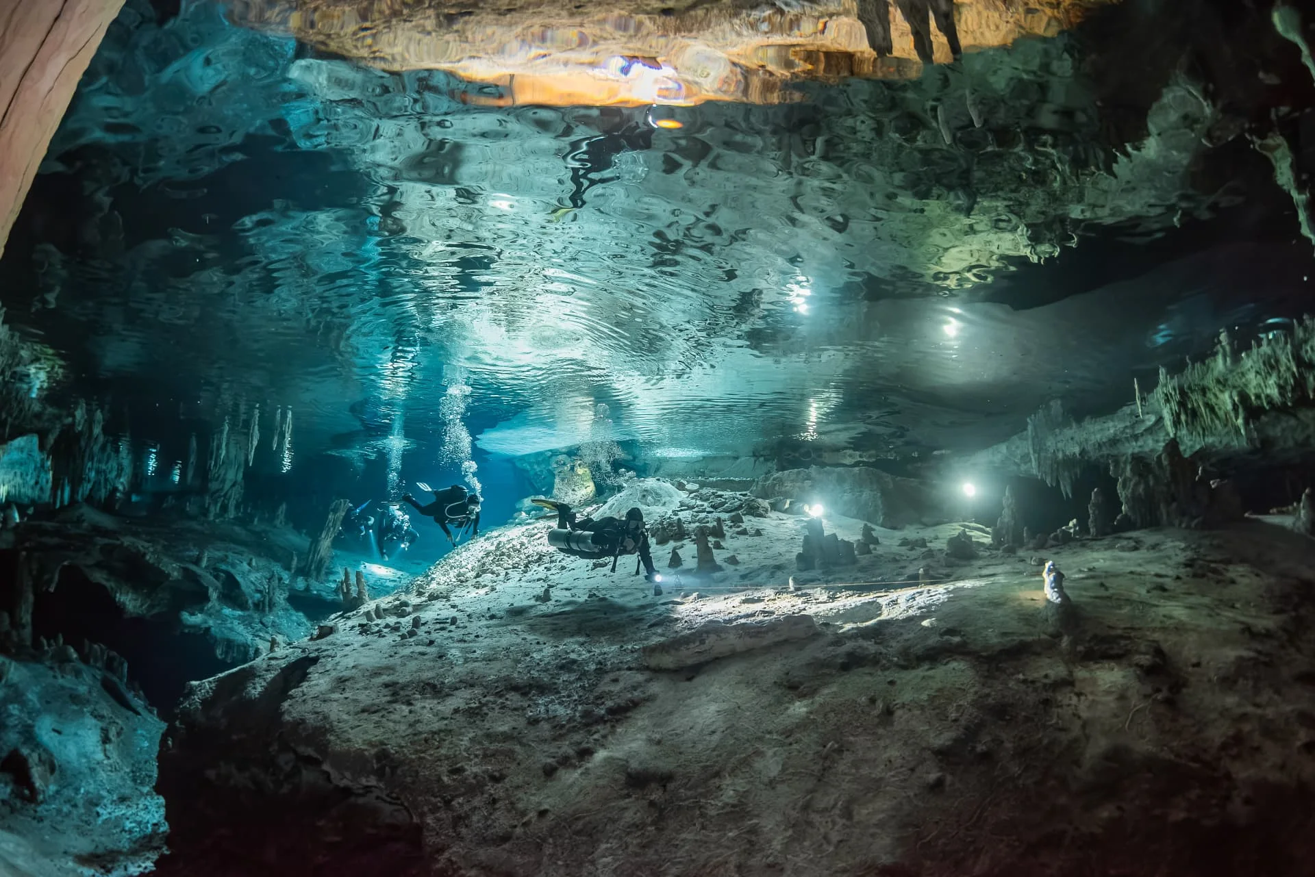 Divers using lights above pale limestone formations at Nohoch Nah Chich