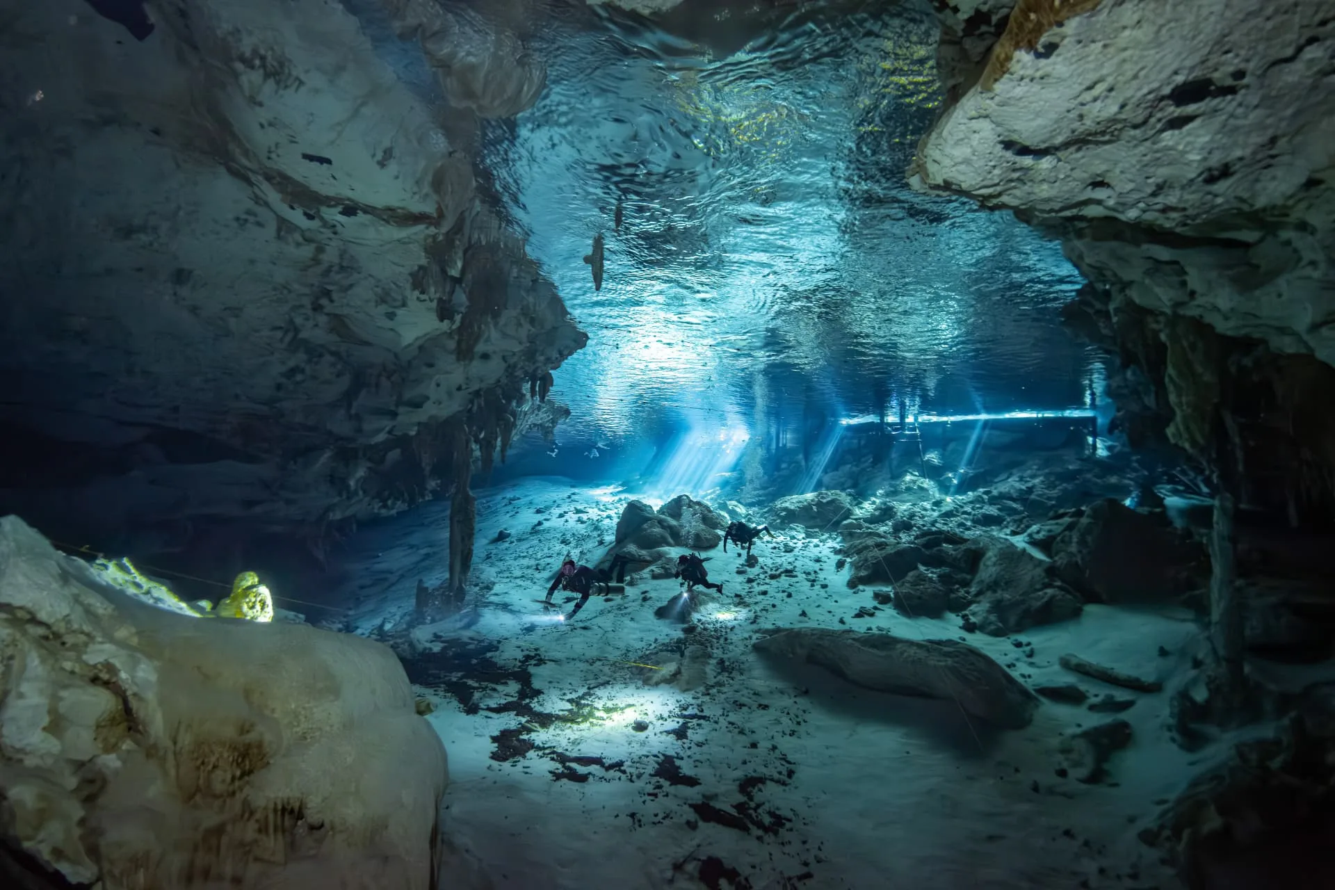 Divers swimming between pale limestone formations at Dos Ojos
