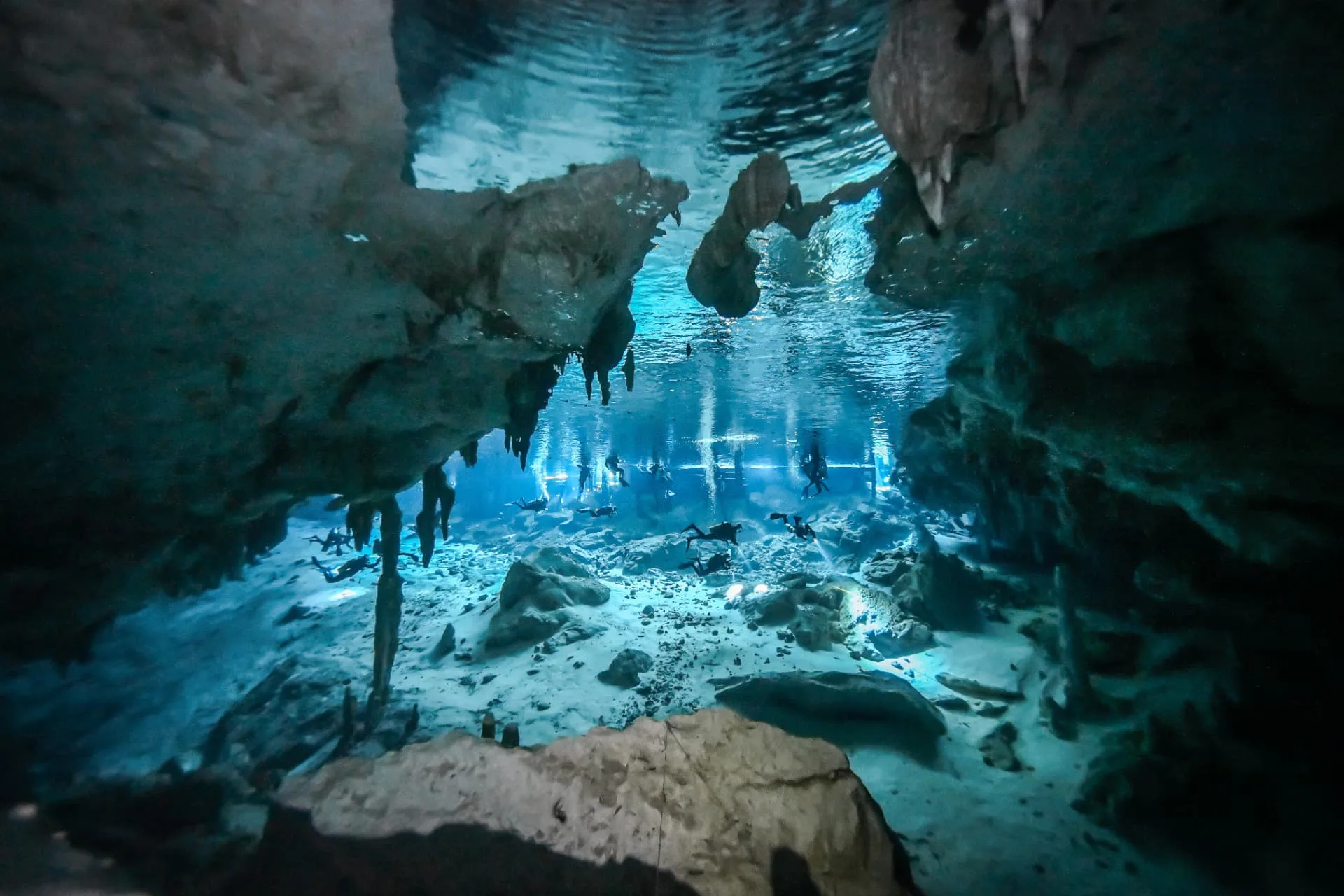 Scuba divers crossing a bright limestone cavern framed by dark underwater rock