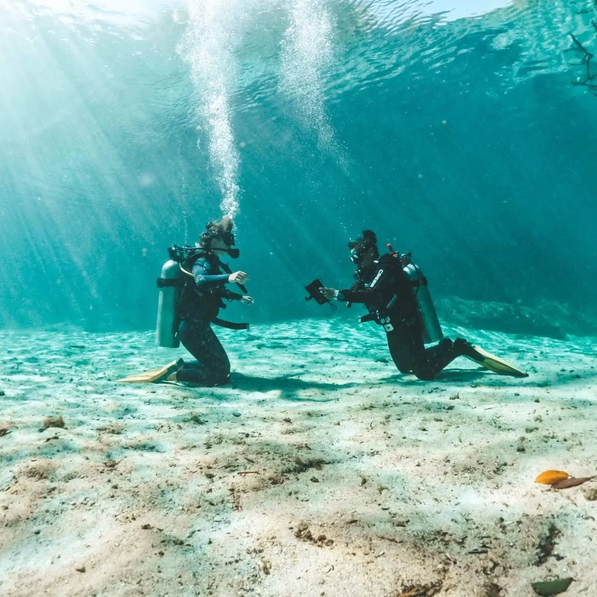 Two scuba divers facing each other while practicing on a shallow sandy bottom
