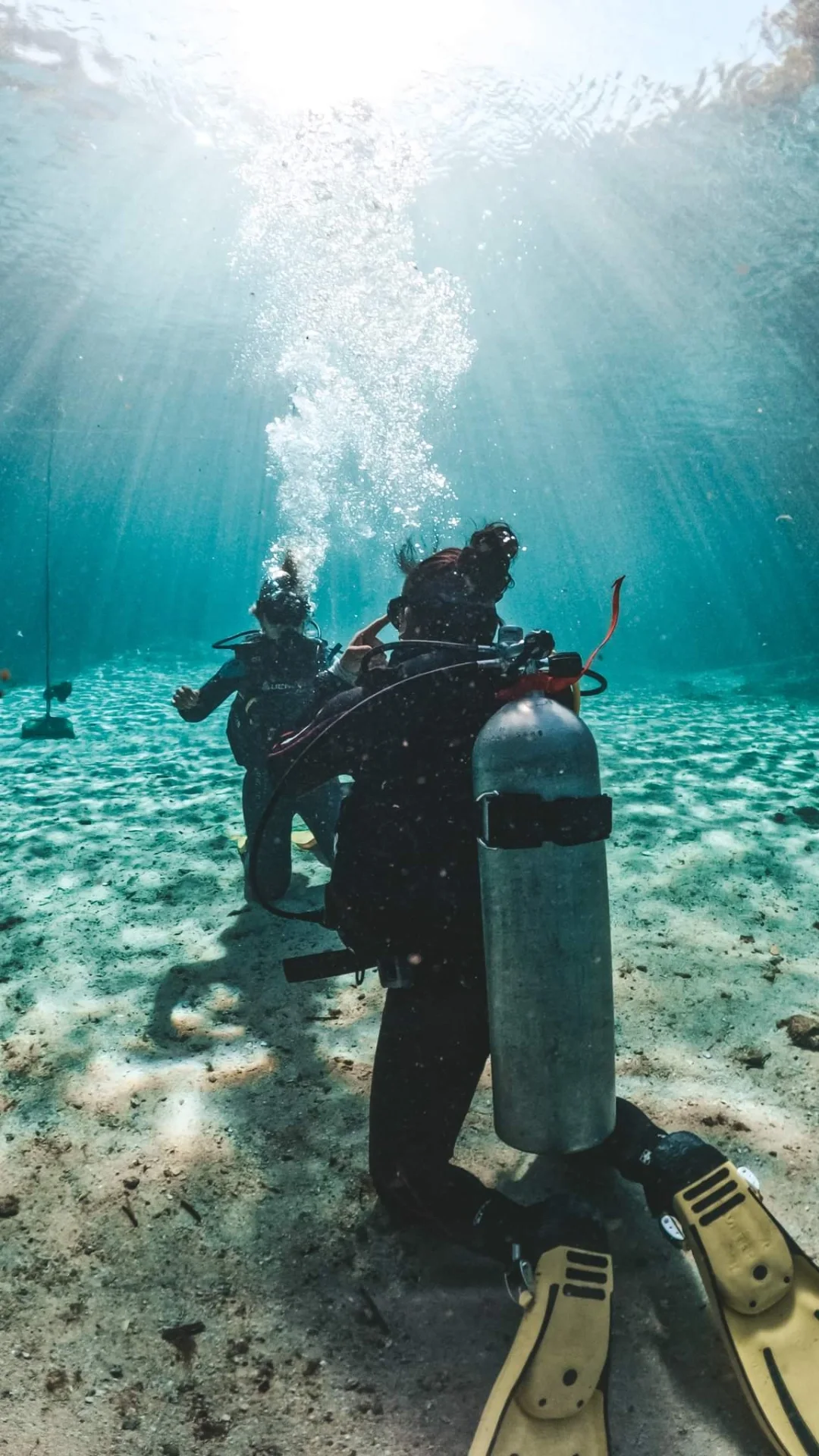 Divers resting on a sandy bottom in calm, shallow, clear water