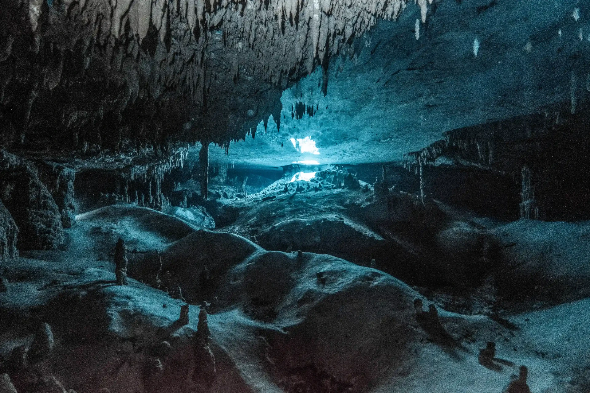 Dark underwater cavern lined with stalactites and pale sand formations